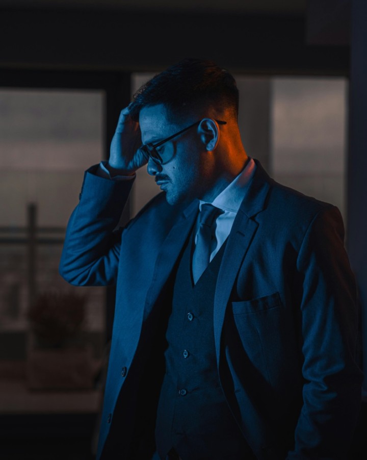 Mann mit Brille und Anzug hält eine Hand an die Stirn im blauen Licht